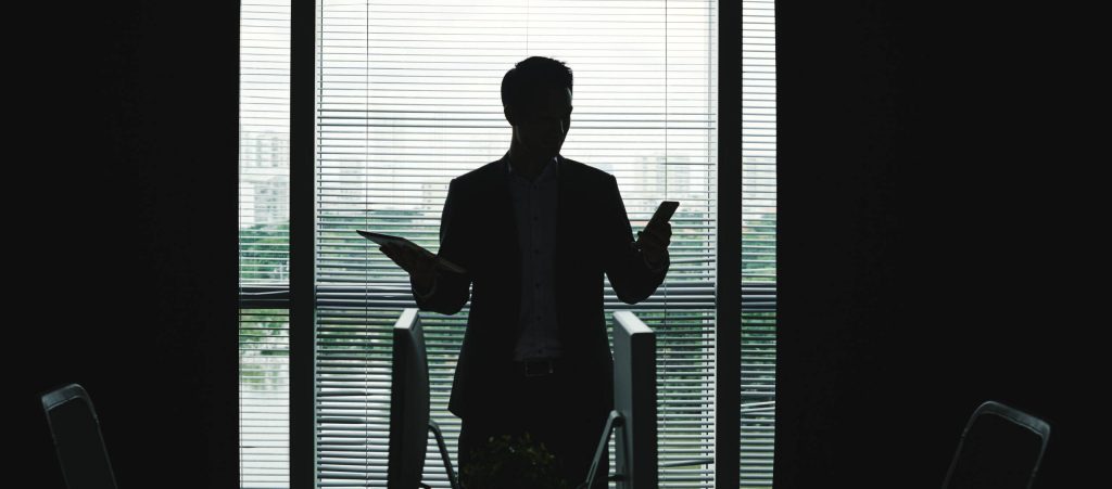 Silhouette of businessman with smartphonew in one hand and digital tablet in another